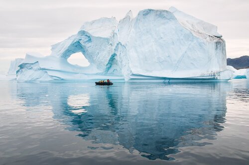 Tourists in Inflatable Rubber Boat in front of weathered iceberg, Scoresby Sund, Greenland