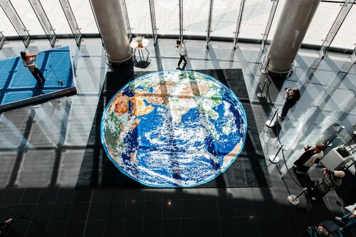 Astana, Kazakhstan — Kazakh artist Alina Akhmetbek presents 72 Voices of Earth, a monumental large-scale quilling mosaic that merges paper art, environmental symbolism,  and conceptual storytelling into a single immersive artwork. The project was publicly demonstrated on April 22, 2026, in celebration of Earth Day, as a World Guinness Records attempt to create the largest paper quilling mosaic image of Earth.
Measuring 41.66 square meters, the artwork consists of 72 individual pieces and more than 300 hundred thousands of individually hand-rolled paper elements arranged into a highly detailed representation of Earth. Entirely handmade over the course of six years, every quill was rolled by hand and carefully applied onto wooden boards to create the final mosaic. 

The mosaic is structured through two interconnected conceptual systems: the symbolism of the number 72 and the geometry of the logarithmic spiral.